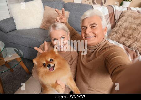 Glückliches Seniorenpaar mit süßem Pommerschen Hund, der zu Hause Selfie macht Stockfoto