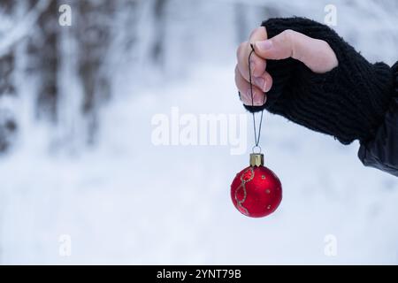 Unerkennbare Frau hängt Weihnachtsdekoration draußen im verschneiten Winterwald. Postkarte Grußkarte Mock Up. Weihnachtsfeier mit rotem Ball, Verzierung Neujahrsfeier Stockfoto
