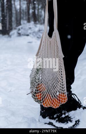 Reife Mandarinen in wiederverwendbarem Netzbeutel draußen im verschneiten Winterwald. Konzept nachhaltiger Weihnachtsfeier, Verantwortung und Inklusivität. Orangen im Baumwollbeutel Stockfoto