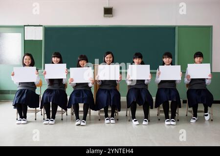 Studentinnen sitzen in einer Reihe und halten ein Brett in einem Klassenzimmer Stockfoto