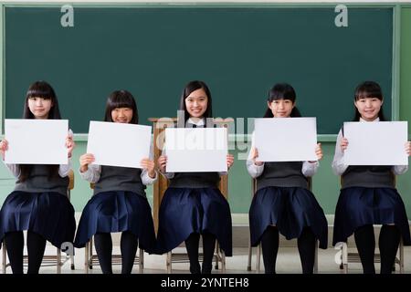 Studentinnen sitzen in einer Reihe und halten ein Brett in einem Klassenzimmer Stockfoto