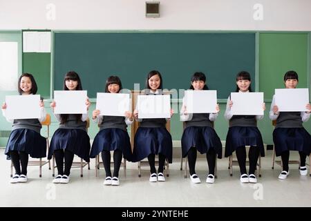 Studentinnen sitzen in einer Reihe und halten ein Brett in einem Klassenzimmer Stockfoto