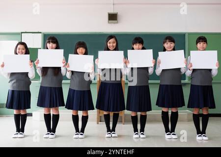 Studentinnen sitzen in einer Reihe und halten ein Brett in einem Klassenzimmer Stockfoto