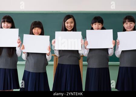 Studentinnen sitzen in einer Reihe und halten ein Brett in einem Klassenzimmer Stockfoto