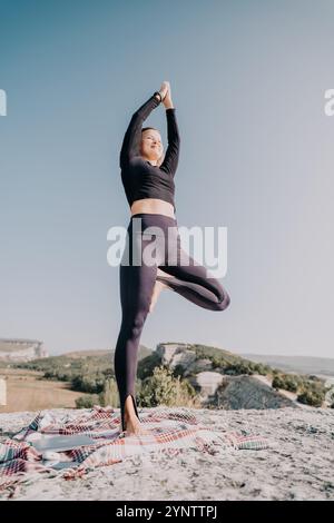 Frau übt Yoga in Baumstellung auf einem Berggipfel Stockfoto