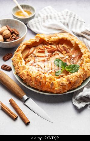 Frisch gebackene Apfelgalette mit Mandelflocken, Zimt und Minze, umgeben von Zutaten und Küchenutensilien Stockfoto