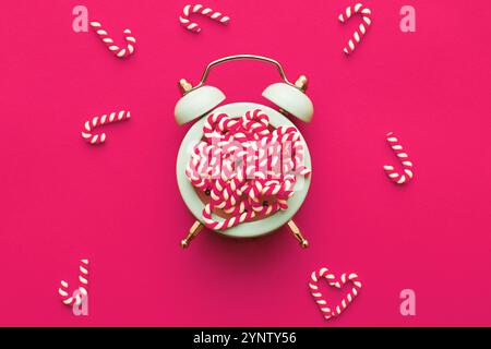 Weihnachtshintergrund mit Zuckerstangen mit dem Wecker auf rosa Hintergrund. Stockfoto