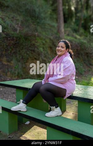 Eine Frau sitzt auf einer Bank mit rosa Hemd und schwarzen Strümpfen. Sie lächelt und genießt ihre Zeit im Freien Stockfoto