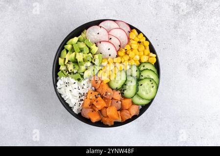 Poke- oder budha-Schüssel mit Lachs, Reis, Gurke, Mais, Rettich, Avocado auf grauem Hintergrund. Draufsicht. Stockfoto
