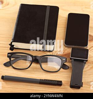 Telefon, Uhr und Brille auf Holzschreibtisch mit Notizbuch, Stift und Tagebuch in der Nähe im Büro für Geschäftsleute. Technologie, Bücher und mobiler Bildschirm auf dem Tisch Stockfoto
