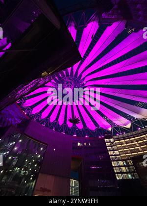 A vibrant purple canopy Sony Center in Berlin illuminates the night sky above modern urban architecture. The intricate geometrical design creates a ca Stockfoto