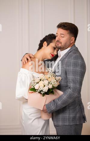 Der Bräutigam umarmte die Braut sanft. Die Braut hält einen Strauß rosa Rosen in den Händen. Stockfoto