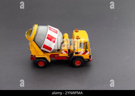 Gelber Zementmischer-Spielzeugwagen mit roten Akzenten auf grauem Hintergrund mit Kopierraum. Stockfoto