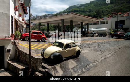 Ein alter Volkswagen Käfer steht an einem steilen Hang in Taxco de Alarcon, Mexiko. Die malerische Straße ist von traditionellen Gebäuden gesäumt, die geschmückt sind Stockfoto