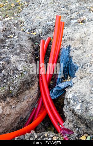 Bündel roter Kunststoffrohre für die elektrische Erdleitung im Freien im Graben Stockfoto