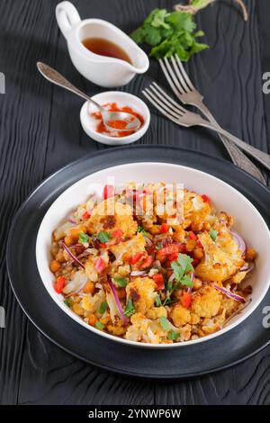 Gebratener Blumenkohl-Quinoa-Salat mit Walnüssen, rotem Pfeffer, Zwiebeln und Koriander in weißer Schüssel auf schwarzem Holztisch mit Gabeln, vertikale Ansicht, Stockfoto