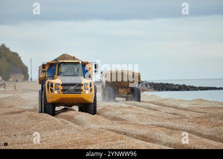 Zwei Volvo A40E Kipper fahren einander vorbei und transportieren Schindeln am Sandgate Beach in der Nähe von Folkestone, Großbritannien. Ein Lkw hat seine Ladung zum Strand geliefert und kehrt zum Nachfüllen zurück. Der Schindel wird jedes Jahr recycelt und bewegt den Schindel entlang der Küste von Ost nach West, um Überschwemmungen und Küstenerosionen zwischen Folkestone und Hythe zu reduzieren. Stockfoto