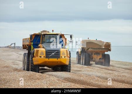 Zwei Volvo A40E Kipper fahren einander vorbei und transportieren Schindeln am Sandgate Beach in der Nähe von Folkestone, Großbritannien. Ein Lkw hat seine Ladung zum Strand geliefert und kehrt zum Nachfüllen zurück. Der Schindel wird jedes Jahr recycelt und bewegt den Schindel entlang der Küste von Ost nach West, um Überschwemmungen und Küstenerosionen zwischen Folkestone und Hythe zu reduzieren. Stockfoto