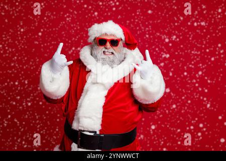 Portrait von attraktiven verrückten Santa zeigt Horn Symbol mit Spaß Neujahr Gelegenheit isoliert über hellen roten Hintergrund Stockfoto