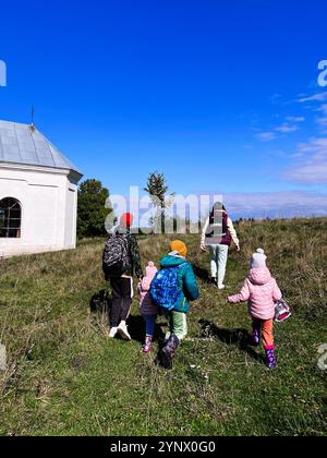 Eine Familie genießt eine gemütliche Wanderung durch ein grünes Feld an einem klaren, sonnigen Tag. Die Szene fängt die Freude des Outdoor-Abenteuers und der Zweisamkeit in Natu ein Stockfoto