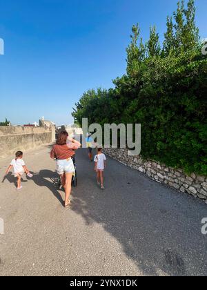 Eine Familie macht einen gemütlichen Spaziergang an einem sonnigen Tag und genießt die Natur. Kinder spielen und erkunden, während ein Erwachsener einen Kinderwagen entlang des Weges schiebt. Nin, Stockfoto