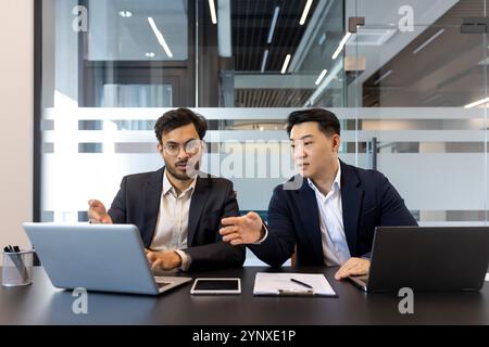 Geschäftsleute, die im modernen Büro mit Laptop- und Smartphone-Technologie eine gemeinsame Diskussion führen. Teamarbeit und Strategie werden im Meeting betont. Stockfoto