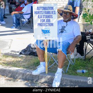 NEW ORLEANS, LA, USA - 2. OKTOBER 2024: Streikende Hafenarbeiter der International Longshoremen's Association sitzen auf dem Bürgersteig und halten ein Streikschild auf der Tchoupitoulas Street am Eingang zum Hafen von New Orleans Stockfoto