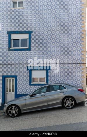 Costa Nova, Portugal - 11. September 2024 : Ein elegantes silbernes Auto parkt neben einem bunten blau-weiß gekachelten Haus. Stockfoto