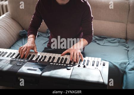 Mann, der eine digitale Tastatur in entspannter Atmosphäre spielt, auf einem Sofa sitzt, in dem natürliches Licht einströmt, und ein ruhiges und fokussiertes musikalisches M einfängt Stockfoto