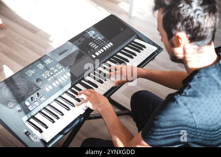 Mann, der eine digitale Tastatur in entspannter Atmosphäre spielt, auf einem Sofa sitzt, in dem natürliches Licht einströmt, und ein ruhiges und fokussiertes musikalisches M einfängt Stockfoto