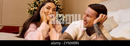 Ein liebevolles Paar genießt einen zärtlichen Moment zusammen an einem wunderschön geschmückten Weihnachtsbaum. Stockfoto