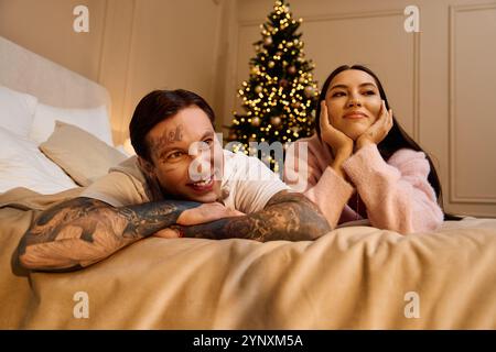 Ein Paar entspannt sich auf einem Bett und genießt die Gesellschaft der anderen neben einem wunderschön geschmückten Baum. Stockfoto