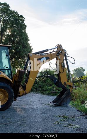 Der Sturm ist vorbei, jetzt wartet ein großer gelber Baggerlader auf der Straße vor einem umgestürzten Baum. Die Reinigungsarbeiten werden bald beginnen. Stockfoto