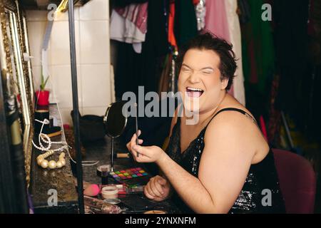 Eine Drag Queen schminkt sich freudig vor einer Weihnachtsshow in einem lebhaften Ankleidezimmer. Stockfoto