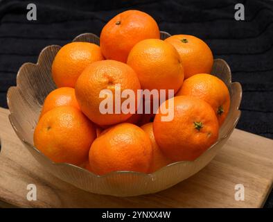 Eine Schüssel mit lebhaften Clementinen steht auf einer Holzoberfläche. Die helle Frucht bildet einen Kontrast zum dunklen Hintergrund und sorgt für eine optisch ansprechende Di Stockfoto