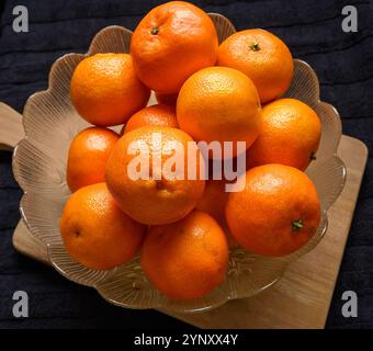 Eine Schüssel mit lebhaften Clementinen steht auf einer Holzoberfläche. Die helle Frucht bildet einen Kontrast zum dunklen Hintergrund und sorgt für eine optisch ansprechende Di Stockfoto