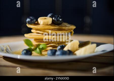 Ein köstlicher Stapel Pfannkuchen mit frischen Blaubeeren und Bananenscheiben, getränkt mit Sirup. Die perfekte Frühstücksumgebung mit warmen Speisen Stockfoto