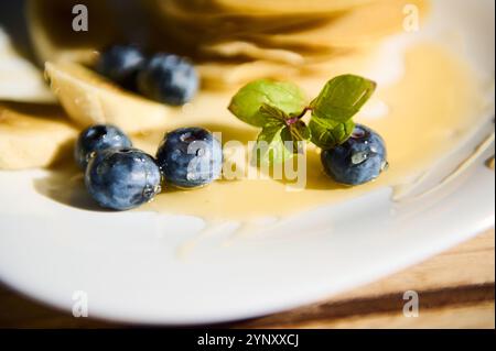 Eine detaillierte Ansicht von frischen Heidelbeeren und Minzblättern auf Pfannkuchen mit Sirup. Sonnenlicht verstärkt die lebendigen Farben und fängt die Frische ein Stockfoto