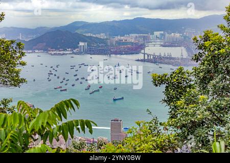 Luftaufnahme von Frachtschiffen, die in der Nähe des Hafens von Hongkong vor Anker liegen, mit städtischer Skyline und Bergen im Hintergrund während des Tages Stockfoto