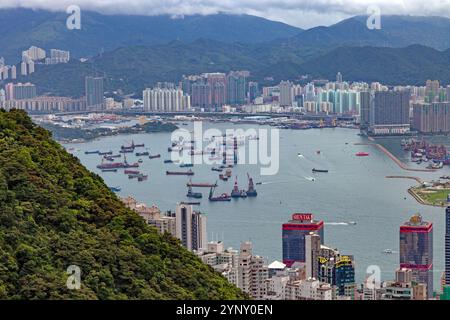 Luftaufnahme von Frachtschiffen, die in der Nähe des Hafens von Hongkong vor Anker liegen, mit städtischer Skyline und Bergen im Hintergrund während des Tages Stockfoto