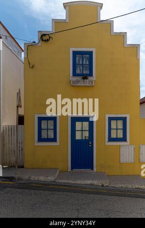 Ein bezauberndes gelbes Haus hat blaue Fenster und einen Balkon in einer ruhigen Gegend. Stockfoto