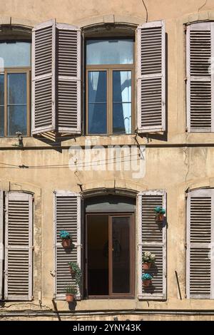 Nahaufnahme der Fenster eines alten Gebäudes mit Holzläden und Topfpflanzen. Der verwitterte Look und das natürliche Licht sorgen für eine warme, nostalgische Atmosphäre Stockfoto