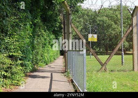 Gosport, Hampshire, England. 4. August 2024. Ein schmaler, von Bäumen gesäumter Fußweg der Grange Road zwischen dem MOD-Grundstück und dem Werksgelände von Huhtamaki. Stockfoto