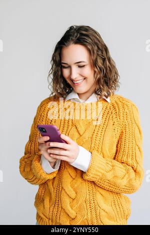 Lächelnde Frau Mit Smartphone. Eine fröhliche junge Frau mit lockigem Haar, die ein Smartphone benutzt. Ideal für die Darstellung moderner Kommunikation, Technologie oder Stockfoto