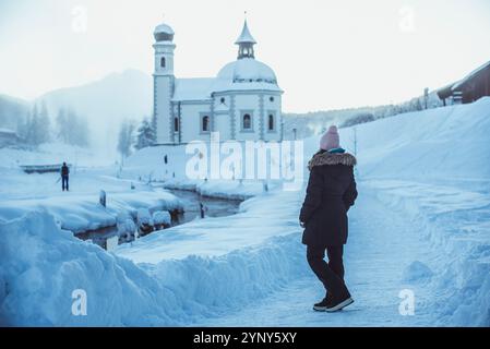 Frau, die im Winterschnee steht, sieht Seekirchl (Heiligkreuzkirchein), Seefeld, Tirol, Österreich Stockfoto
