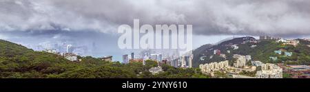 Panoramablick auf die Skyline von Hongkong, umgeben von üppigen grünen Hügeln und einem geschäftigen Hafen im Sommer Stockfoto