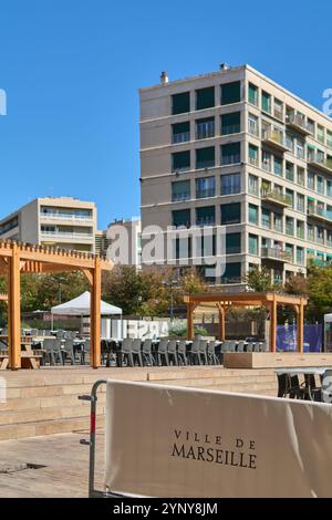 Marseille. Frankreich - 27. November 2024: Sitzbereich im Freien in Marseille mit Holzpflaugen, modernen Stühlen und einem Stadtgebäude im Hintergrund Stockfoto