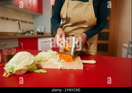 Eine Person reift Karotten in einer gemütlichen Küche, umgeben von frisch gehacktem Kohl. Die lebhaften Farben und das zwanglose Ambiente erwecken das Gefühl der Hausmannskost Stockfoto