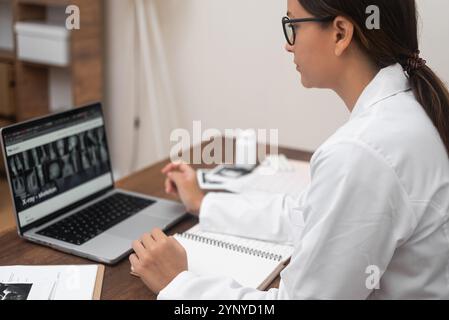 Der Radiologie-Arzt in Brille untersucht Röntgenbilder, die auf einem Laptop-Bildschirm angezeigt werden, mit einem fokussierten Blick. Stockfoto