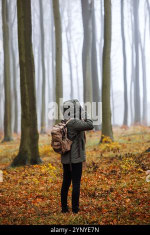 Wandern im Herbst. Frau mit Rucksack geht durch nebeligen Buchenwald. Touristen tragen Jacke mit Kapuze bei kaltem Wetter in der Herbstsaison Stockfoto